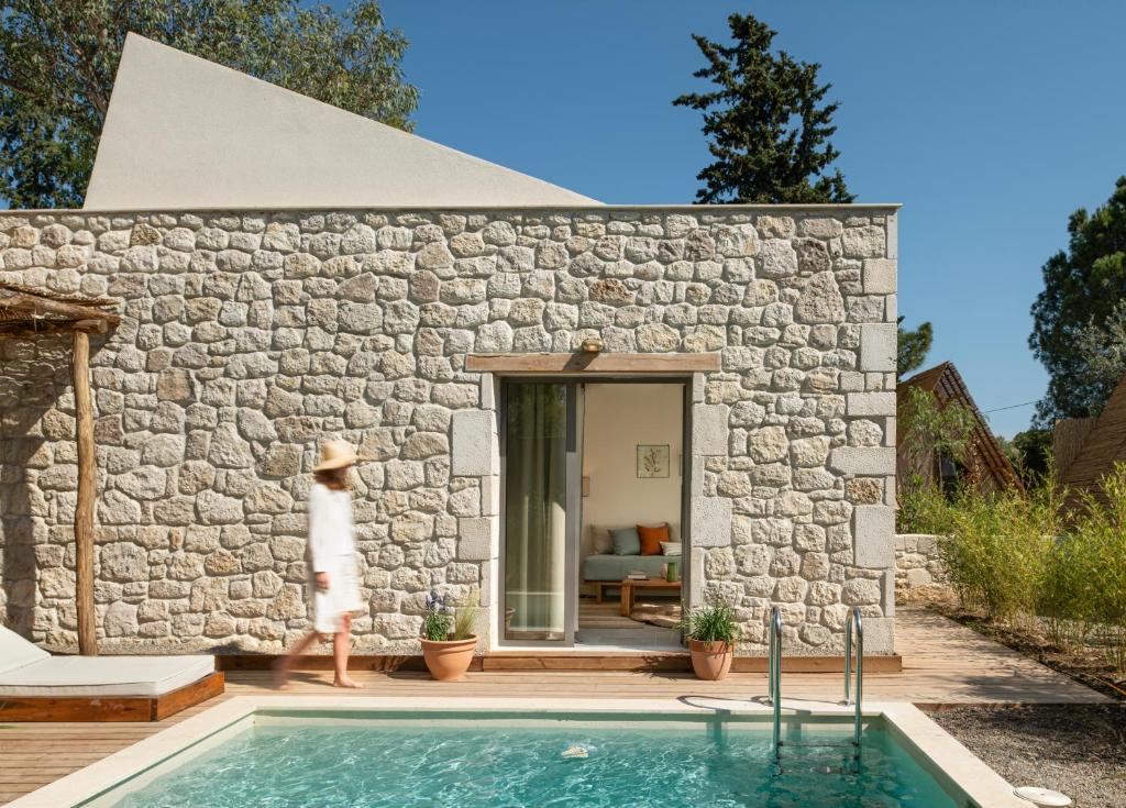 a woman standing in front of a stone house with a swimming pool at Ergon Beach House Nikiti in Nikiti