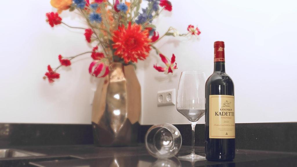 een fles wijn naast een glas en een vaas met bloemen bij Luxe woning ‘BARNS’ Castricum aan Zee + airco + parkeren in Castricum