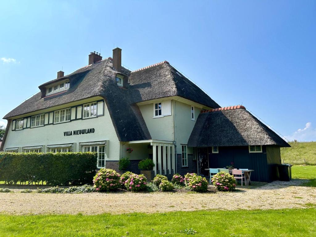 een groot wit huis met een rieten dak bij Villa Nieuwland B&B in Den Oever