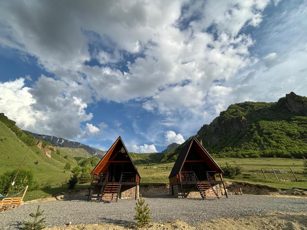 due capanne di paglia in un campo con montagne sullo sfondo di Gagma chalets a Kazbegi