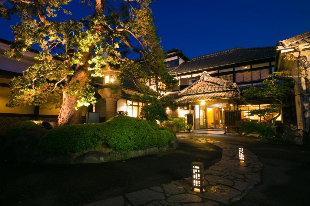 un edificio con un árbol delante de él por la noche en Ryokan Wataya en Karatsu