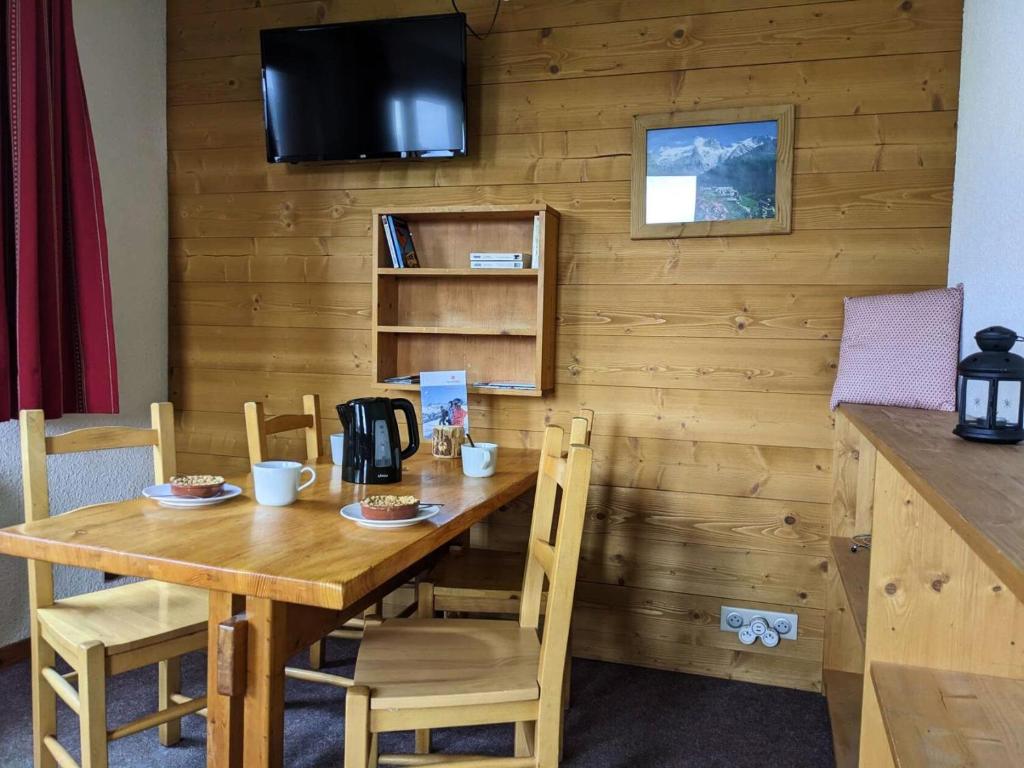 une table en bois avec des chaises et une télévision murale dans l'établissement Résidence Souche - La Souche 10 - Agréable 2 pièces, terrasse skis aux pieds MAE-5114, à Valmorel