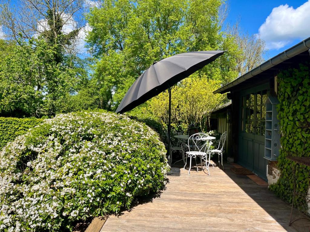 une terrasse avec un parasol noir, une table et des chaises dans l'établissement Paisible cottage au bord de l'eau -15 mn des côtes, à Pierrefitte-en-Auge