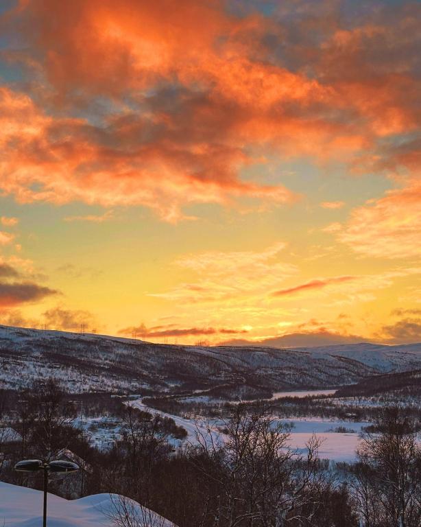 a sunset over a snow covered field with the sky at Skaidi Luxury Lodge – Heart of the Arctic in Hammerfest