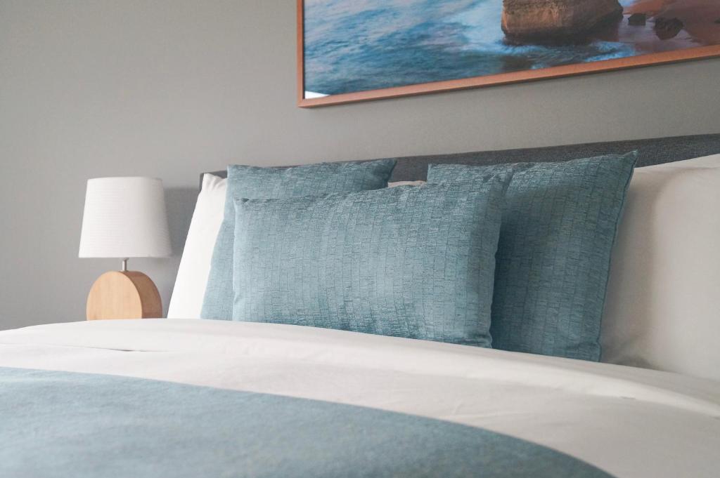 a bed with blue pillows and a picture on the wall at Waves Luxury Suites in Port Campbell