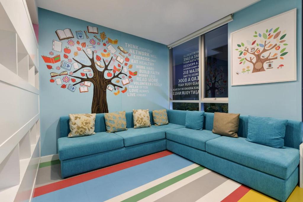 A colorful lounge with a large sectional sofa and illustrated tree mural.