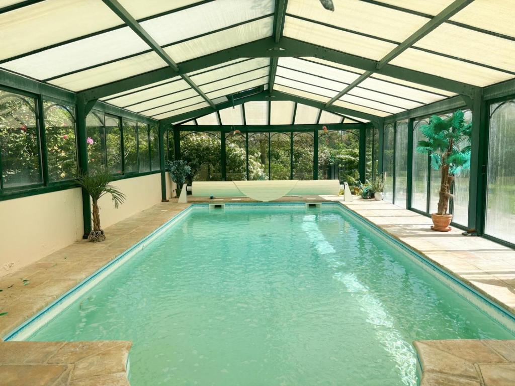 an indoor pool in a conservatory with glass walls at La Maison du Tilleul avec Piscine couverte chauffée in Saint-Sulpice-sur-Risle