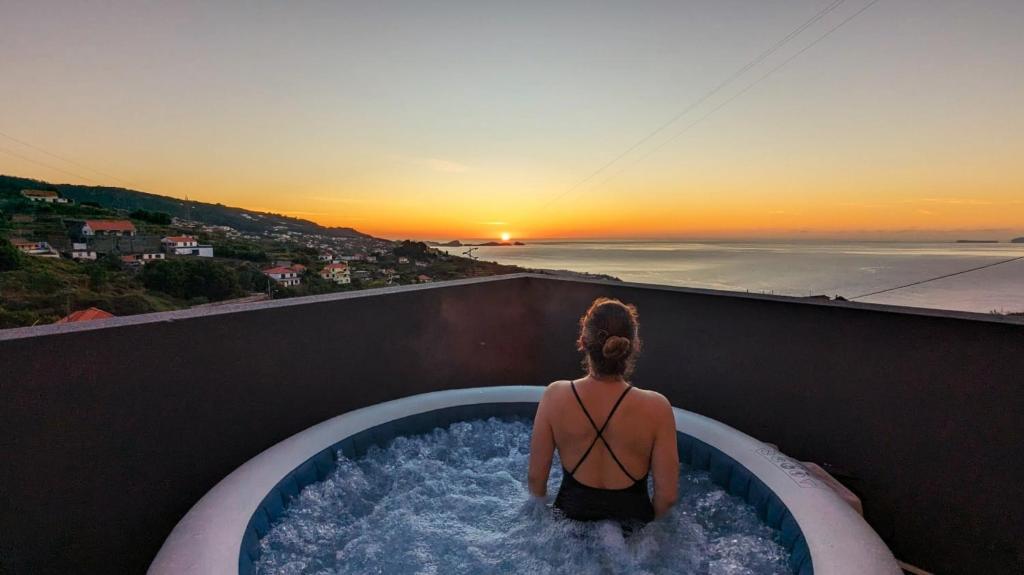 uma mulher em uma banheira de hidromassagem observando o pôr do sol em Ocean Hill House em Santa Cruz - Madeira