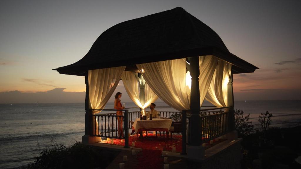 a couple sitting at a table in a gazebo on the beach at Jumeirah Bali in Uluwatu