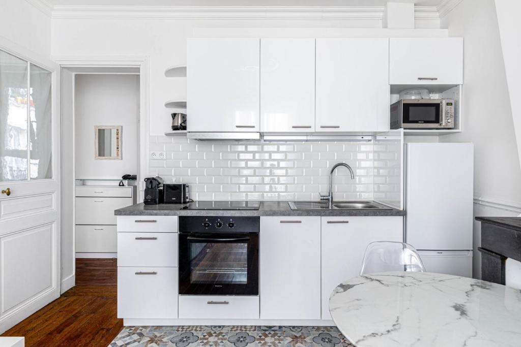 une cuisine blanche avec des armoires blanches et un évier dans l'établissement GuestReady - Apt. Cosy et confortable dans le 10e, à Paris