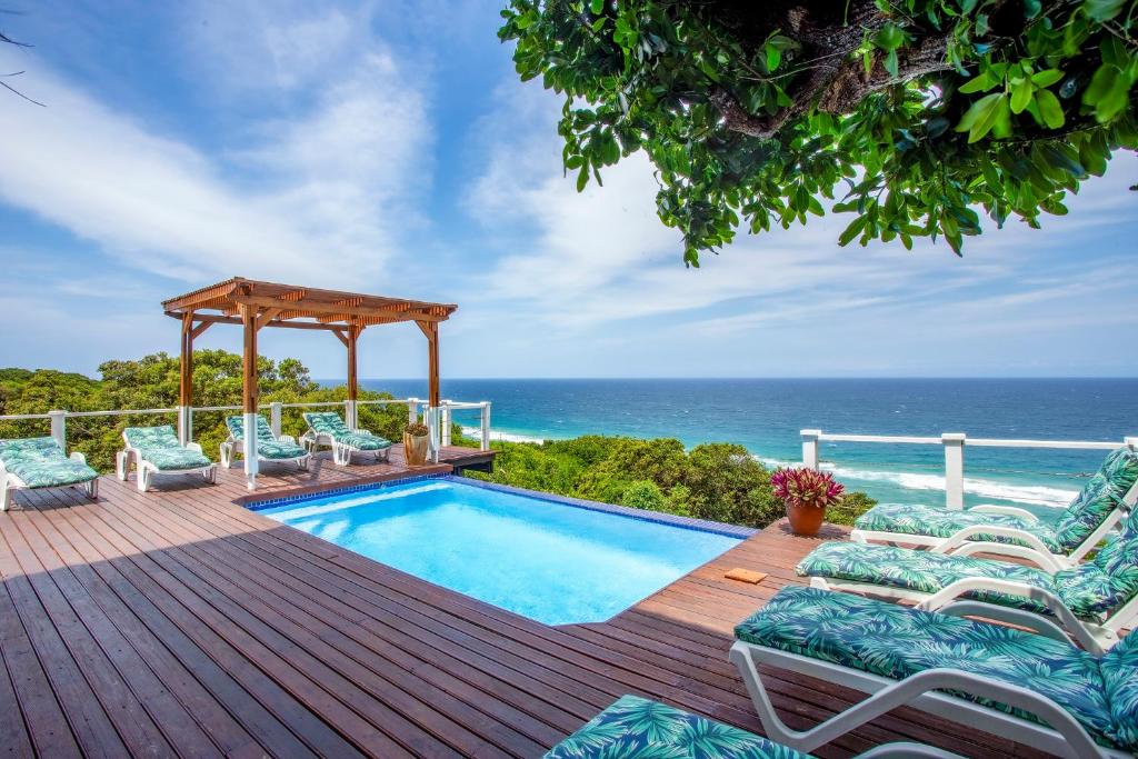 a swimming pool on a deck with chairs and the ocean at Naudicals Dune in Chefe Imala