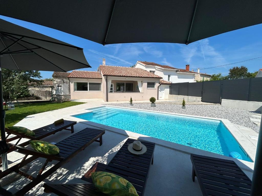 a swimming pool with chairs and an umbrella next to a house at Holiday house Diva with a pool in Svetvinčenat