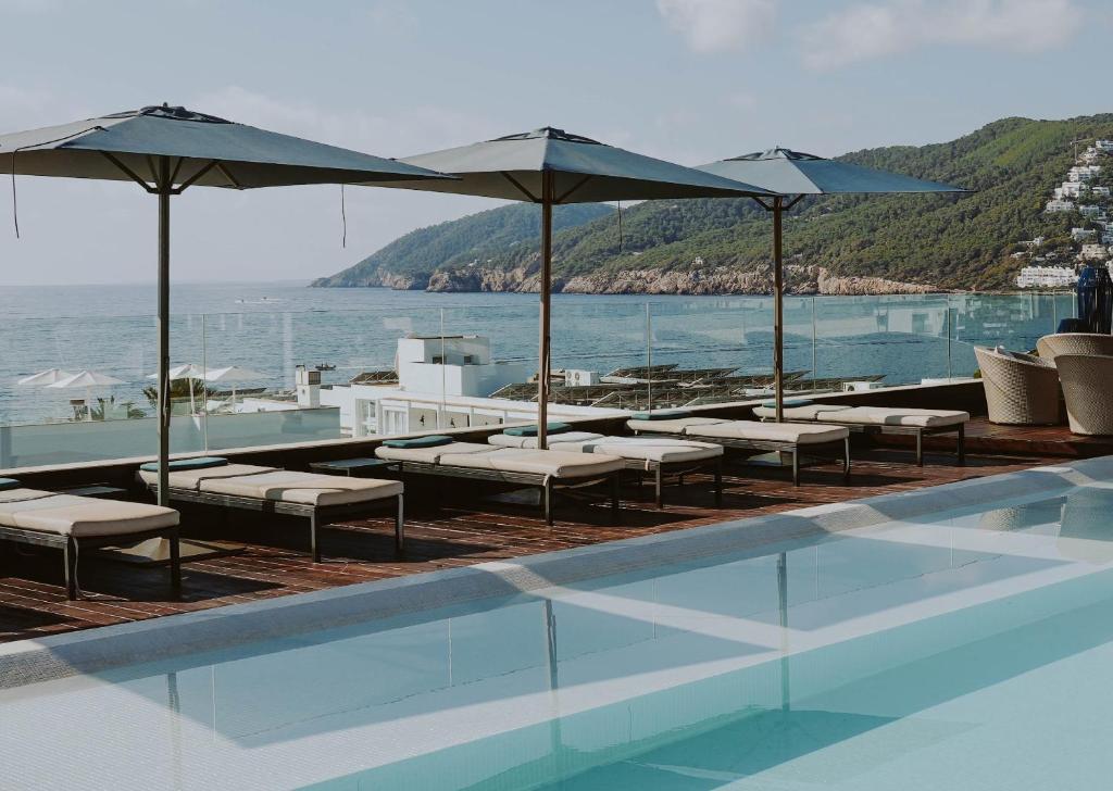 einen Pool mit Stühlen und Sonnenschirmen sowie das Meer in der Unterkunft Aguas de Ibiza Grand Luxe Hotel - Small Luxury Hotel of the World in Santa Eulària des Riu