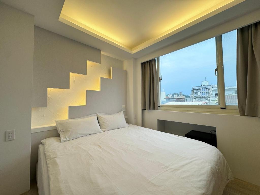 1 dormitorio con cama blanca y ventana grande en 日日藍旅市區民宿, en Hualien City