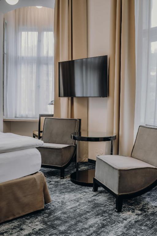 a hotel room with two beds and chairs and a flat screen tv at Esplanade Carlsbad in Karlovy Vary