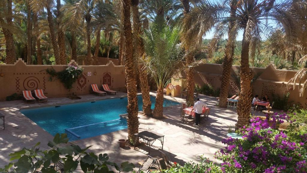 a man standing next to a swimming pool with palm trees at Fibule Du Draa Kasbah D'hôtes in Zagora