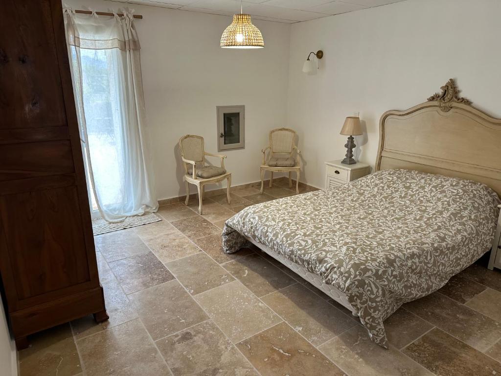 a bedroom with a bed and two chairs and a window at Appartement provençal in Mirabel-aux-Baronnies