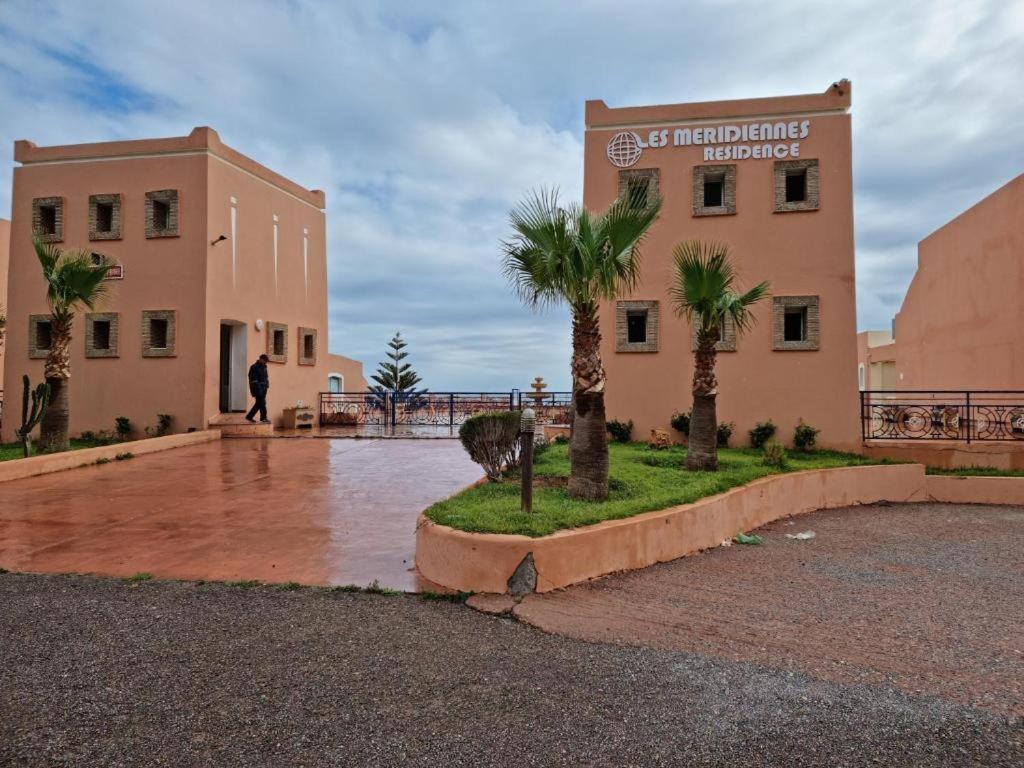 a man walking in front of a building with palm trees at Villa plage tiguert résidence les méridiennes in Agadir