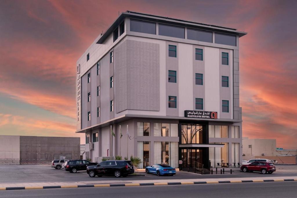 Marvelous Hotel في تبوك: تقديم مبنى فيه سيارات متوقفة في موقف