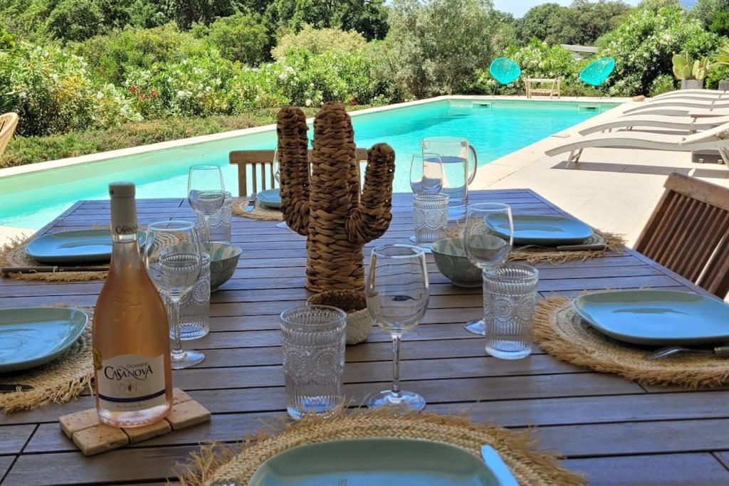 une table avec des verres et une bouteille de vin et un cactus dans l'établissement Villa Olmeccia piscine 14 m, clim, plein Sud, à Porto-Vecchio