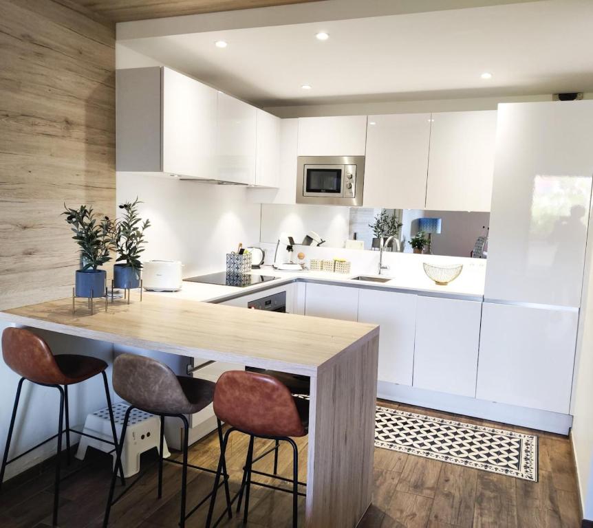 une cuisine avec des placards blancs et une table en bois avec des tabourets dans l'établissement Appartement les Rocades Collioure, à Collioure