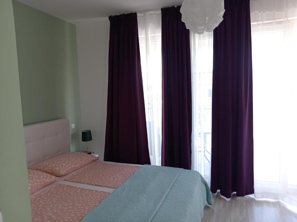 a bedroom with a bed with purple curtains and windows at Ana Rooms in Krk