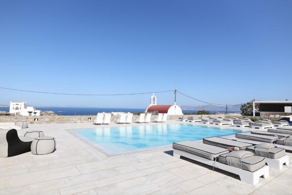 a swimming pool with chaise lounge chairs and the ocean at Margie Mykonos Hotel in Mýkonos City