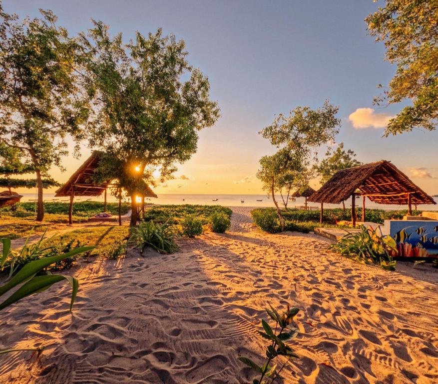 基林多尼的住宿－Maisara Mafia Beach Lodge，日落时分拥有树木和小屋的海滩