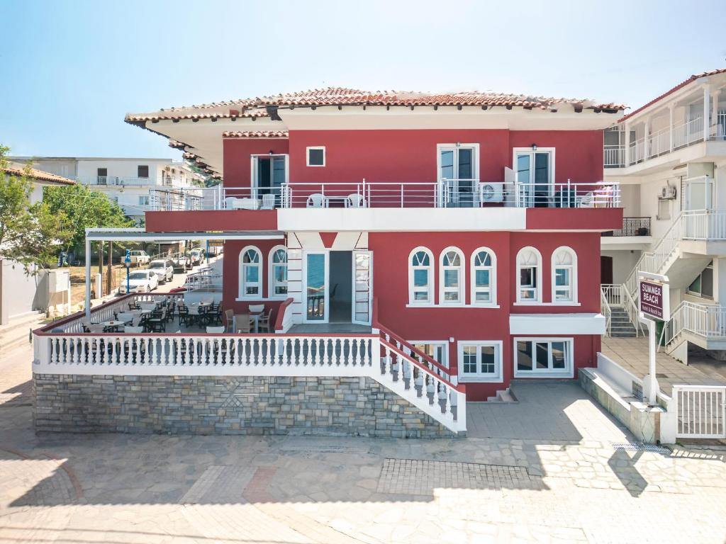 a red building with a balcony on a street at Summer Beach Hotel in Polychrono