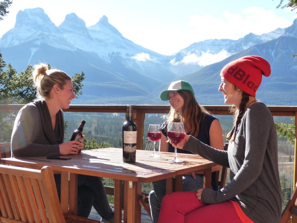 trzy kobiety siedzące przy stole z kieliszkami do wina w obiekcie Canmore Alpine Hostel - Alpine Club of Canada w mieście Canmore