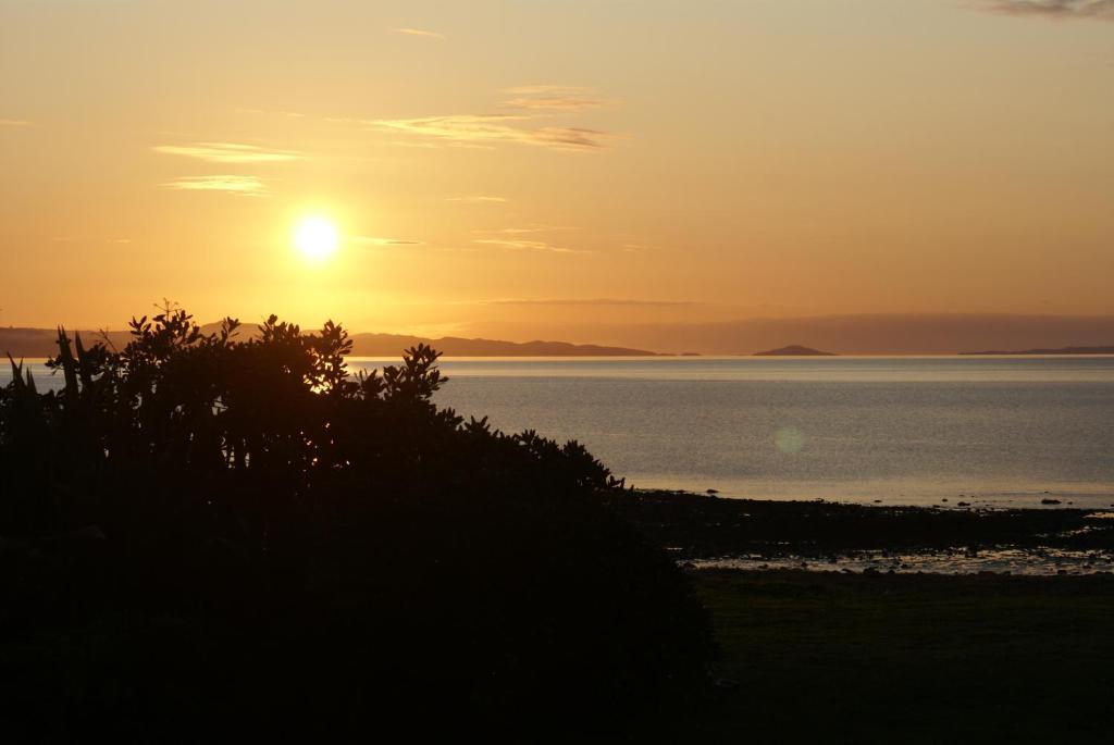 einen Sonnenuntergang über dem Wasser mit der Sonne am Himmel in der Unterkunft Te Puru Beach Lodge in Te Puru