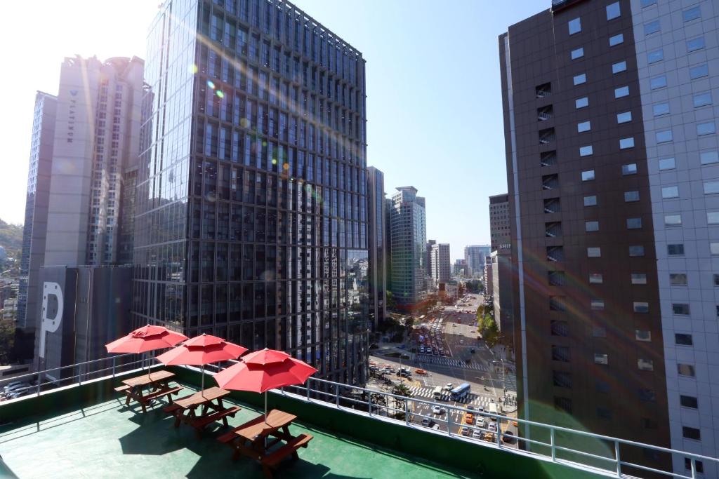 einen Balkon mit Tischen und roten Sonnenschirmen auf einem Gebäude in der Unterkunft 57 Myeongdong Hostel in Seoul