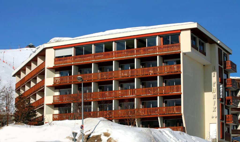 een appartementencomplex met sneeuw ervoor bij Hôtel Eliova Le Chaix in L'Alpe-d'Huez