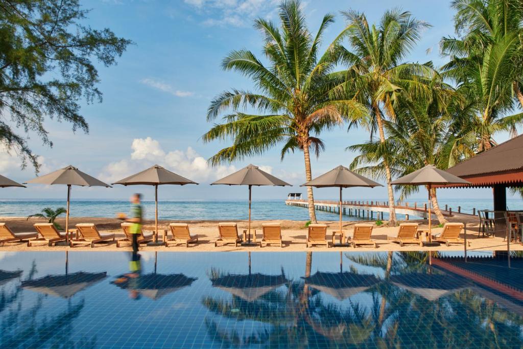 uma piscina com cadeiras e guarda-sóis na praia em The Boathouse Pulau Tioman em Ilha Tioman
