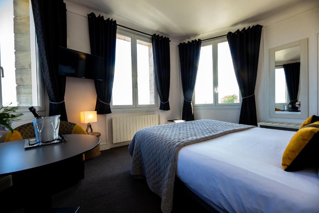 a bedroom with a bed and a desk and windows at La Villa Andry in Ouistreham