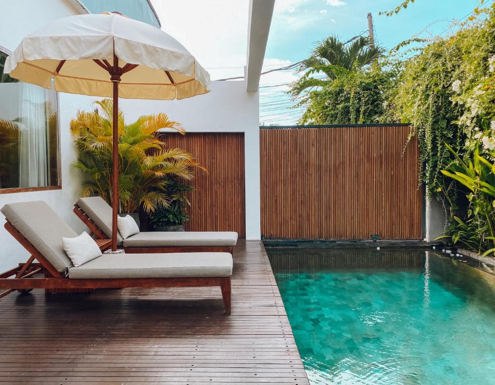a pool with two chairs and an umbrella next to it at Suites Infinity & Beyond in Seminyak