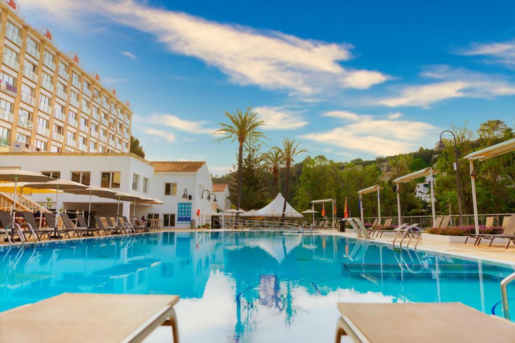 a swimming pool at a hotel with tables and chairs at Minura Cala Galdana & Apartamentos d'Aljandar in Cala Galdana