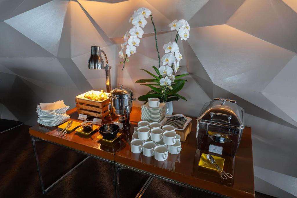 A self-service drinks station with coffee equipment, cups, plates and a flower arrangement.