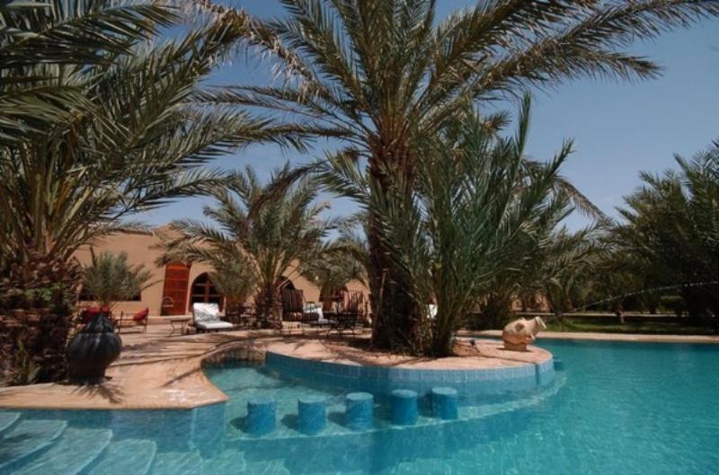 a swimming pool with palm trees in a resort at La Rose Du Desert in Erfoud