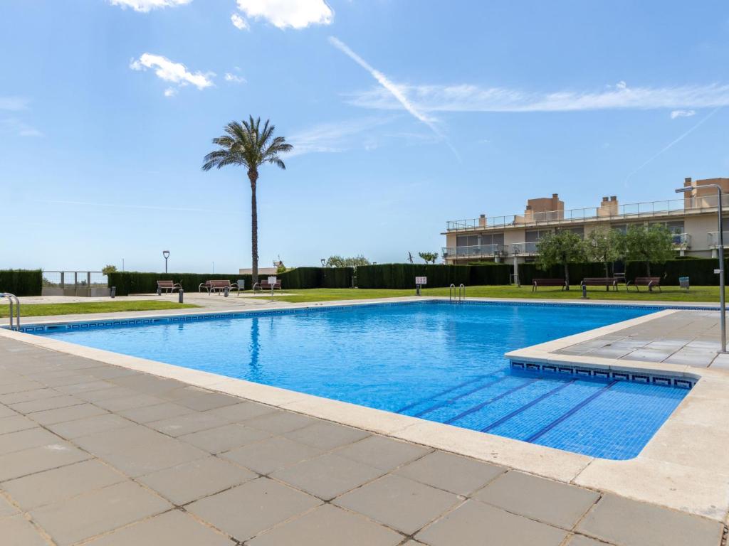 a swimming pool with a palm tree and a building at Apartment Viena 13 by Interhome in L'Ampolla