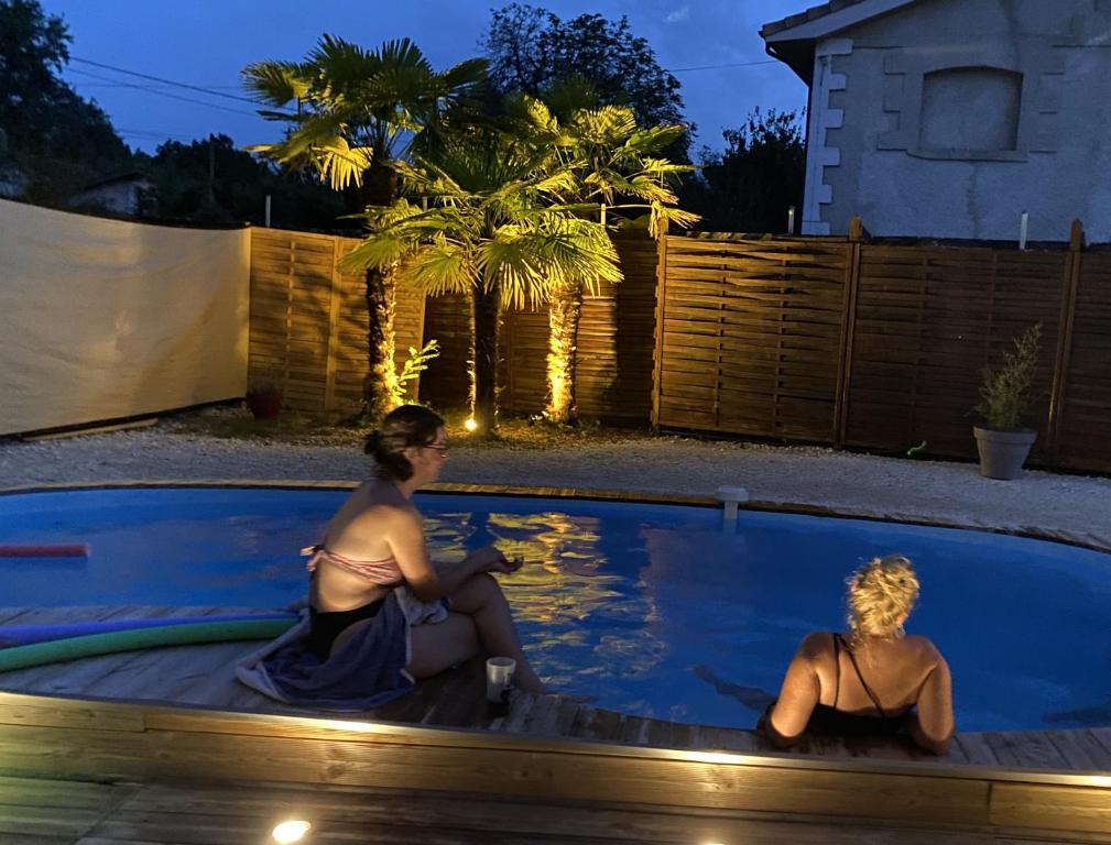 2 femmes assises dans une piscine la nuit dans l'établissement Domaine Shanti Lande, à Ménesplet
