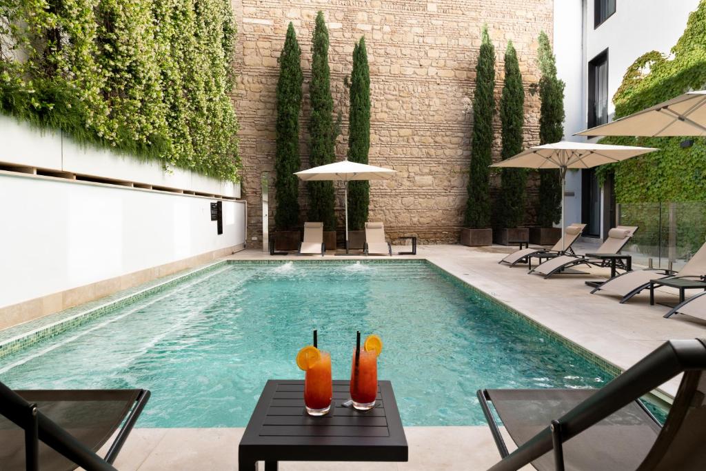 uma piscina com dois cocktails de laranja sobre uma mesa em H10 Palacio Colomera em Córdoba