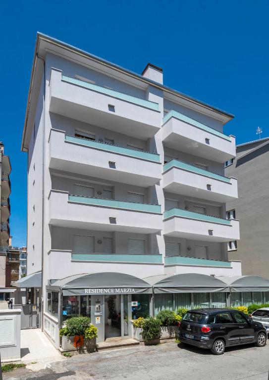 Hotel Residence Marzia, a white building with cars parked in front of it at Residence Marzia in Rimini
