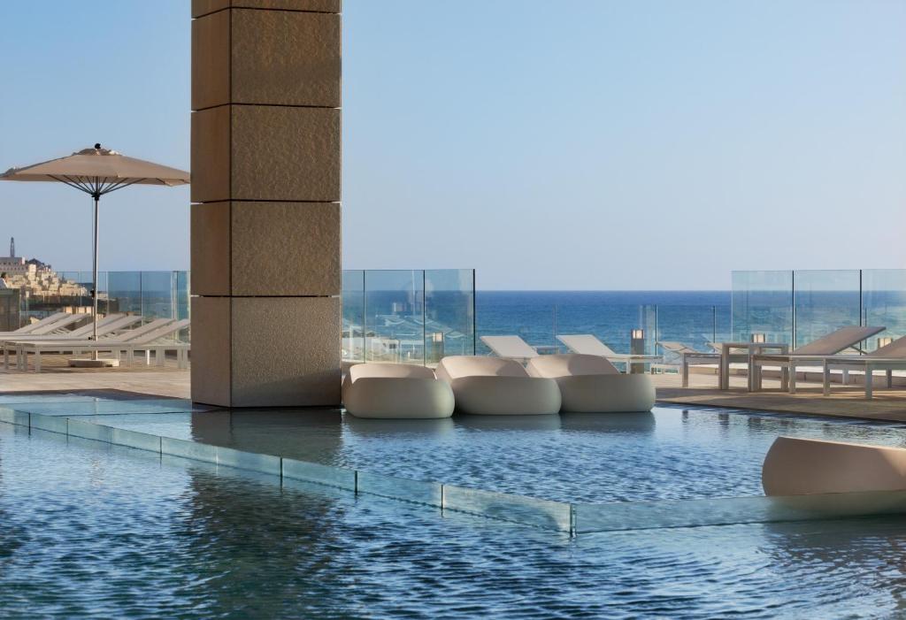 a pool with white chairs and the ocean in the background at Royal Beach Hotel Tel Aviv by Isrotel Exclusive in Tel Aviv