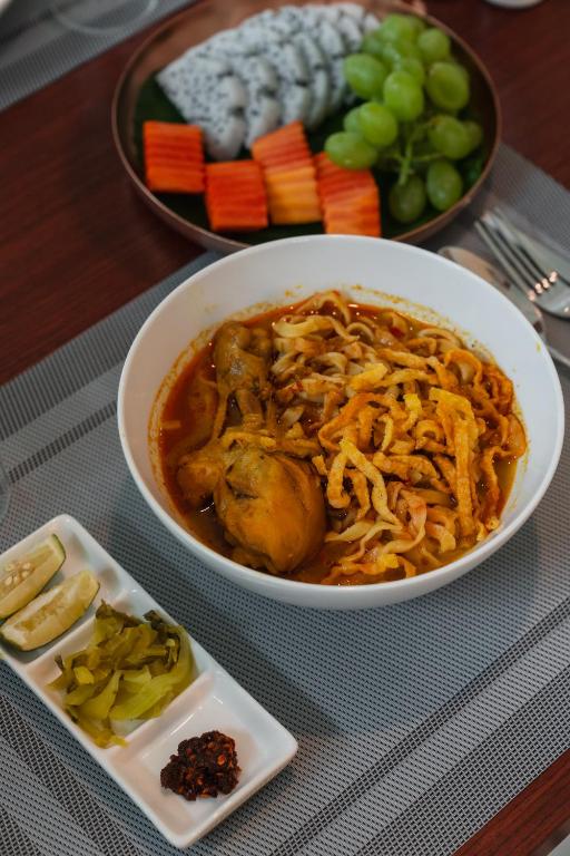 A close-up of a noodle dish served with fruit, vegetables and condiments.