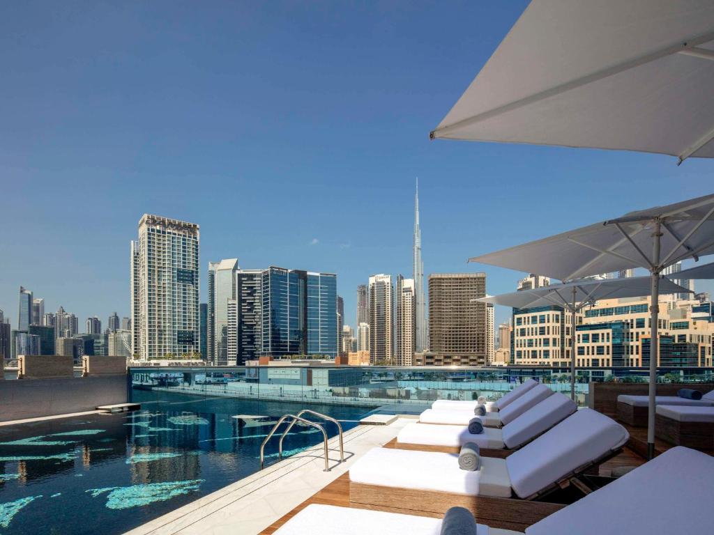 una piscina con sedie a sdraio bianche e uno skyline della città di Hyde Hotel Dubai a Dubai