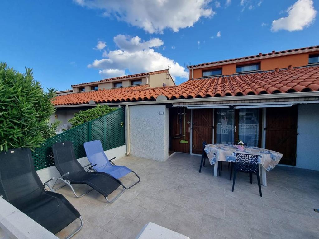 une terrasse avec une table et des chaises ainsi qu'une maison dans l'établissement Charmante Villa T3 avec Piscine, Terrasse et Parking pour 6 Personnes à Port Barcarès - FR-1-81-619, au Barcarès