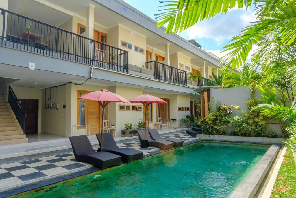 a house with a swimming pool with chairs and umbrellas at Olivia Guest House Canggu in Canggu