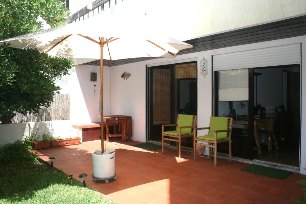 un patio con sombrilla, mesa y sillas en At the beach with a private garden, en Carcavelos