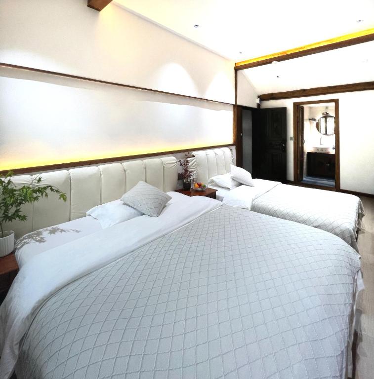 two beds in a hotel room with white sheets at 原乡文苑客栈 in Lijiang